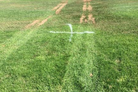 Tractor wheel ruts pressed into a wet sports field, showing compaction and soil displacement from machinery trafficking on saturated ground